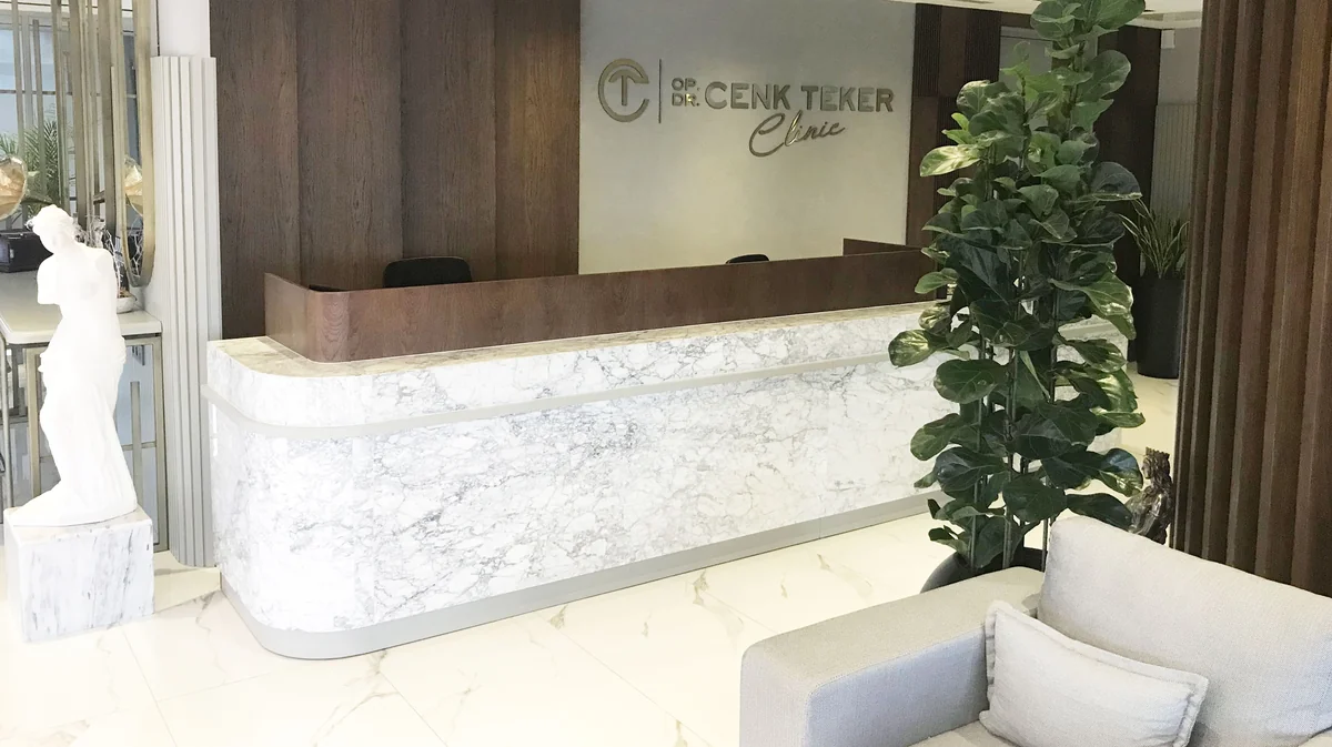 Dr. Cenk Teker Kliniği’nin resepsiyonu: mermer bankosu, ceviz duvarı ve pirinç klinik yazısıyla Bakırköy’deki karşılama alanı
